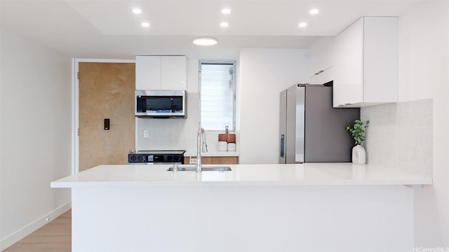 kitchen with a peninsula, a sink, stainless steel appliances, white cabinetry, and light countertops