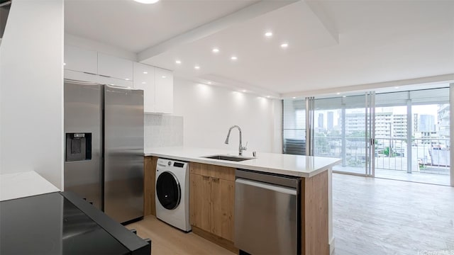 kitchen with a peninsula, a sink, stainless steel appliances, modern cabinets, and washer / clothes dryer