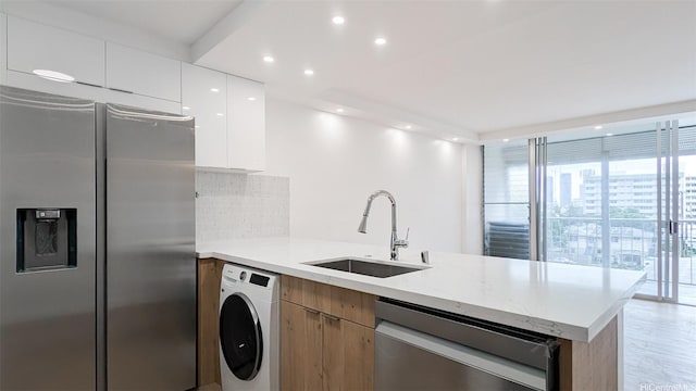 kitchen featuring a sink, a peninsula, washer / dryer, modern cabinets, and appliances with stainless steel finishes
