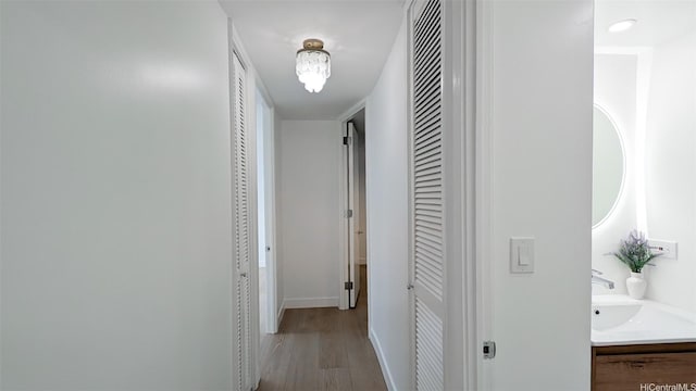 hallway with baseboards, light wood finished floors, and a sink