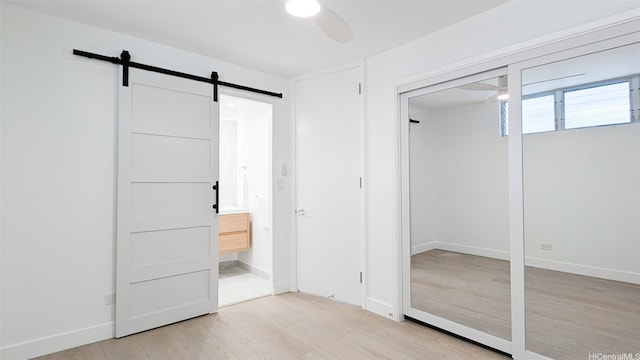 unfurnished bedroom featuring light wood-style floors, a barn door, baseboards, and ceiling fan