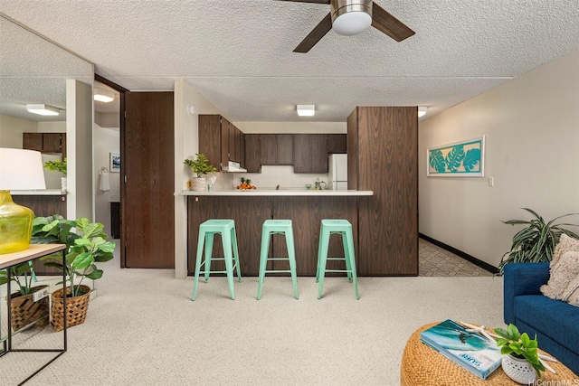 kitchen featuring freestanding refrigerator, a ceiling fan, dark brown cabinets, a breakfast bar, and light countertops
