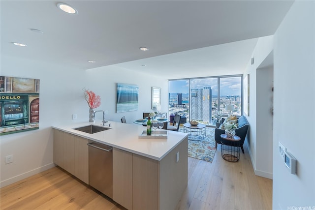 kitchen featuring stainless steel dishwasher, a peninsula, a sink, open floor plan, and light wood-style flooring