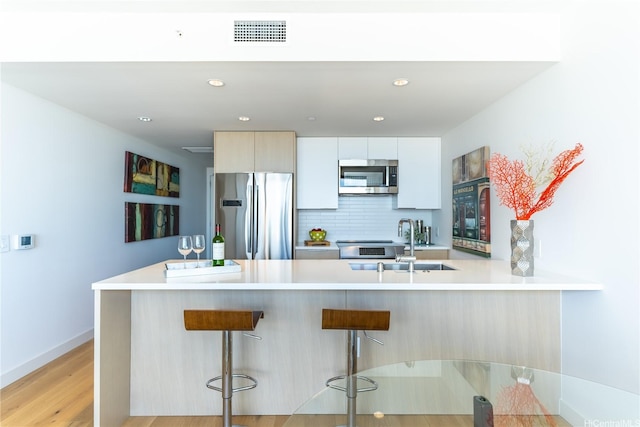 kitchen with stainless steel appliances, a peninsula, a kitchen breakfast bar, light countertops, and recessed lighting