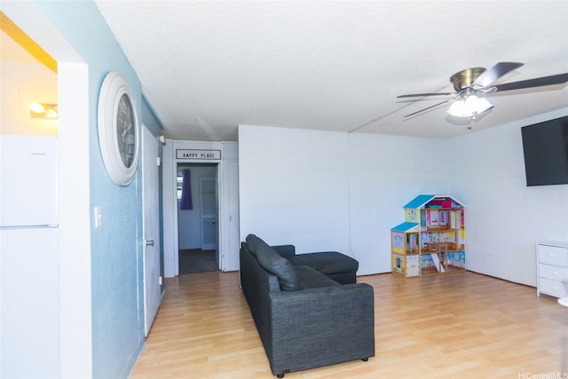 living area featuring a textured ceiling, light wood-type flooring, and a ceiling fan