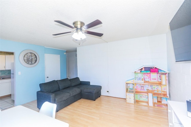 living area featuring a ceiling fan, a textured ceiling, light wood-style flooring, and concrete block wall