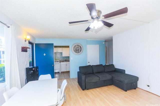 living area featuring ceiling fan, light wood-style flooring, and concrete block wall
