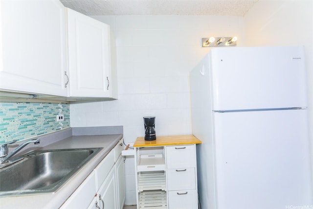kitchen featuring a sink, freestanding refrigerator, white cabinetry, and tasteful backsplash