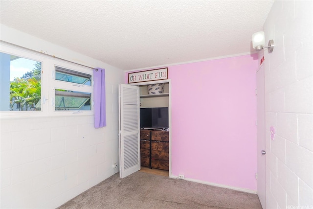 unfurnished bedroom with carpet, a textured ceiling, and concrete block wall