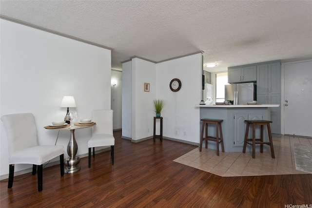kitchen with a textured ceiling, a kitchen bar, stainless steel fridge with ice dispenser, a peninsula, and wood finished floors