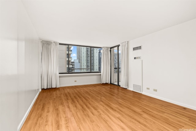 spare room with baseboards, visible vents, light wood-type flooring, and a city view