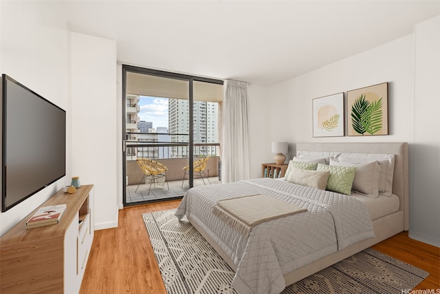 bedroom featuring a city view, light wood-type flooring, access to outside, and a wall of windows