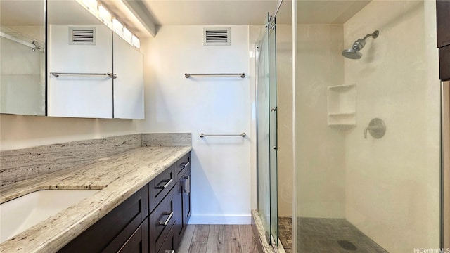 bathroom featuring wood finished floors, a shower stall, vanity, and baseboards