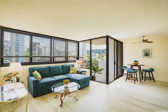 living area with a textured ceiling, wood finished floors, a ceiling fan, and a wall of windows