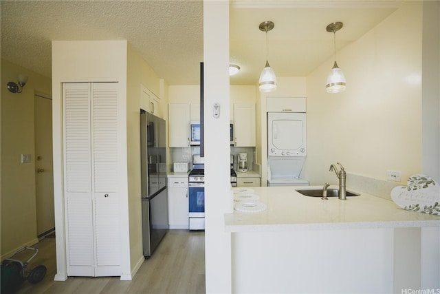 kitchen featuring a sink, stainless steel gas range, stacked washer and clothes dryer, a peninsula, and light wood finished floors