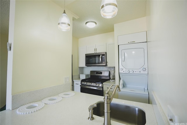kitchen with appliances with stainless steel finishes, stacked washer and clothes dryer, light countertops, a sink, and white cabinets