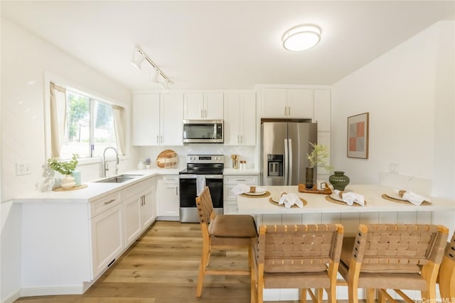 kitchen with appliances with stainless steel finishes, a sink, a peninsula, white cabinets, and a breakfast bar area