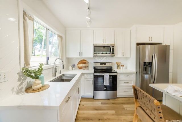 kitchen featuring appliances with stainless steel finishes, a sink, white cabinetry, and light wood-style floors