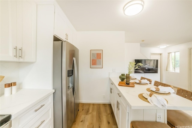 kitchen with stainless steel refrigerator with ice dispenser, a kitchen breakfast bar, a peninsula, light wood-style floors, and white cabinetry
