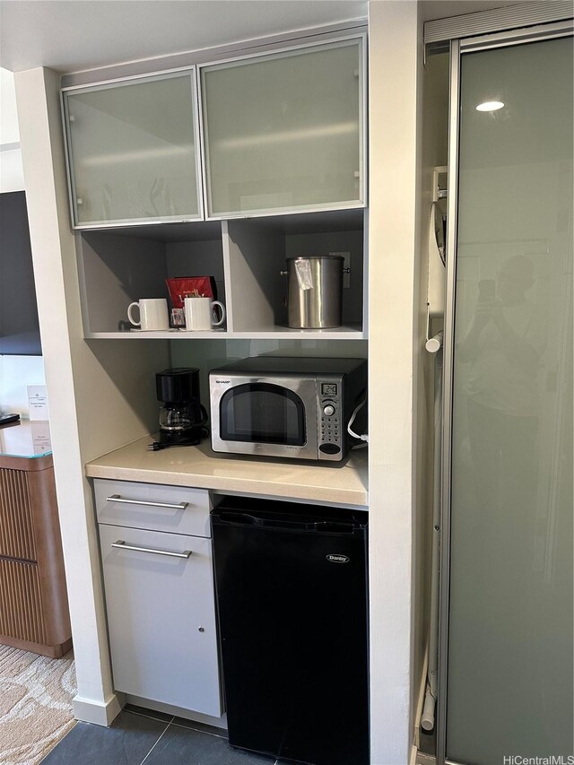 bar featuring stainless steel microwave, fridge, freestanding refrigerator, and tile patterned floors