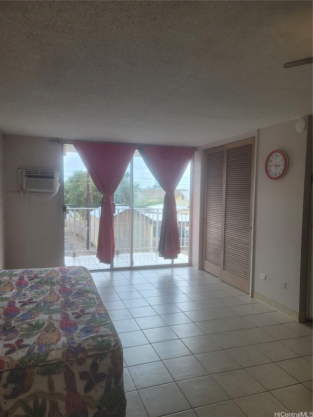 bedroom with light tile patterned floors, a wall mounted air conditioner, a textured ceiling, and access to exterior