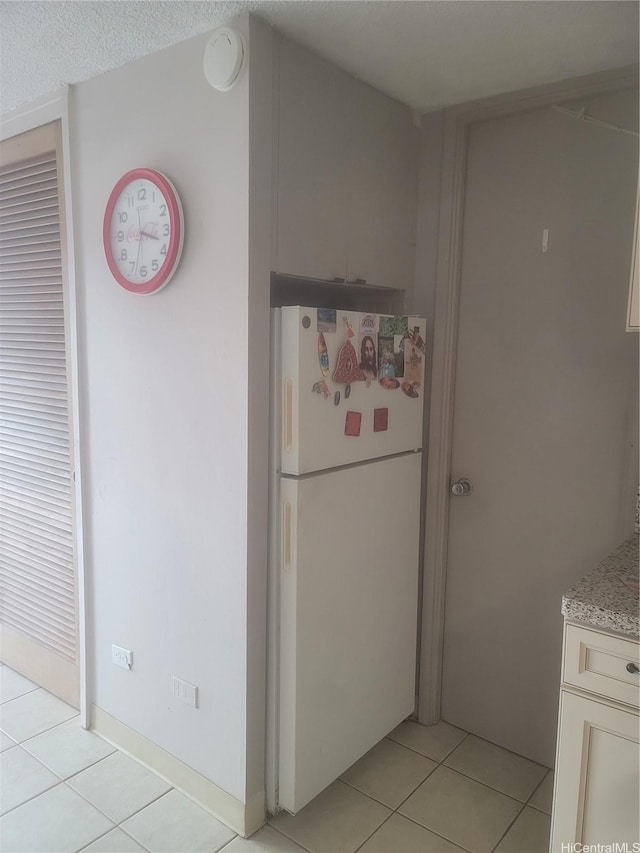 kitchen with freestanding refrigerator, light stone counters, and light tile patterned floors