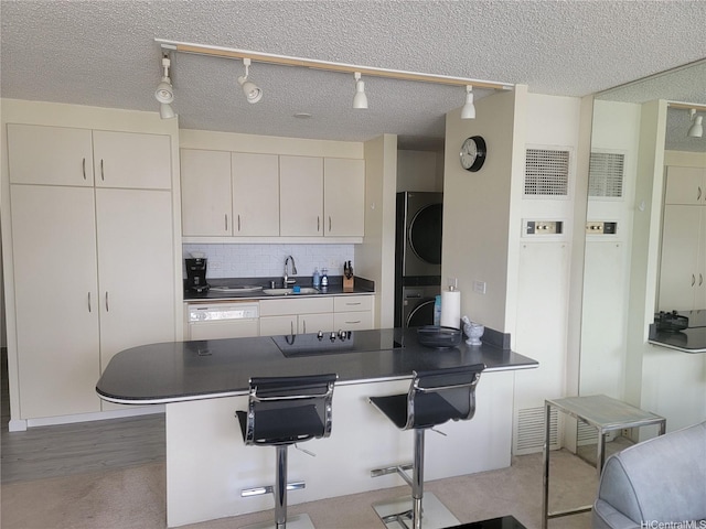 kitchen featuring stacked washer / dryer, dark countertops, a kitchen bar, backsplash, and a peninsula