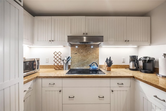 kitchen with stainless steel microwave, under cabinet range hood, white cabinetry, light countertops, and black electric cooktop