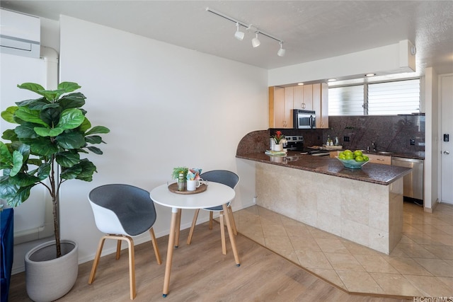 kitchen with a wall mounted AC, track lighting, a peninsula, decorative backsplash, and stainless steel appliances