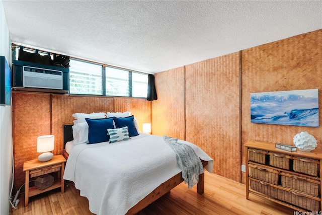 bedroom with a textured ceiling, wood-type flooring, cooling unit, and wood walls