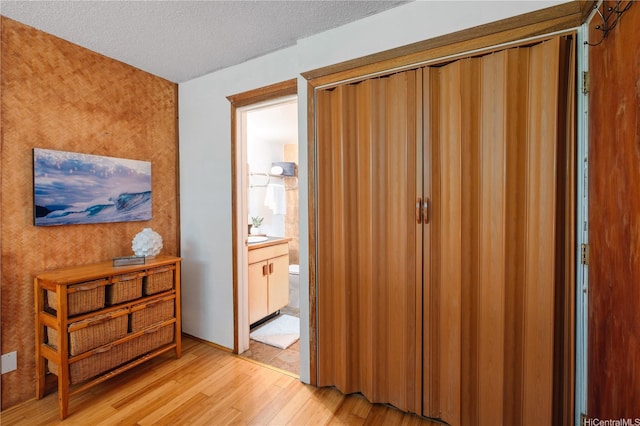 bedroom with a textured ceiling, ensuite bath, and light wood-style floors