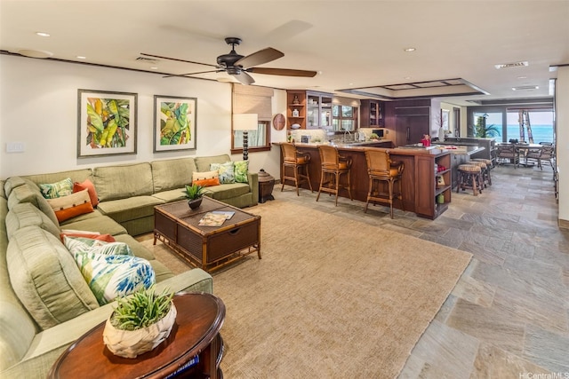 living area with indoor bar, visible vents, ceiling fan, and stone finish floor