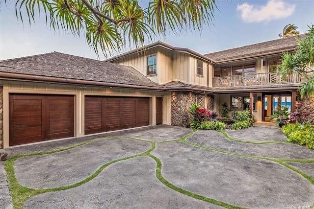 view of front facade with a balcony, a garage, stone siding, and driveway
