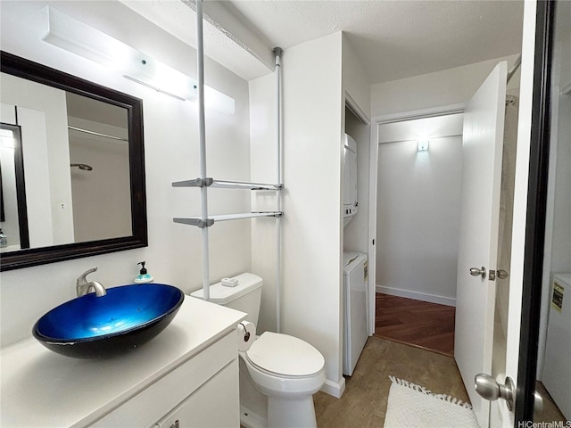 bathroom featuring wood finished floors, toilet, vanity, and estacked washer and dryer