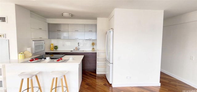 kitchen featuring a kitchen bar, a sink, wood finished floors, and white appliances