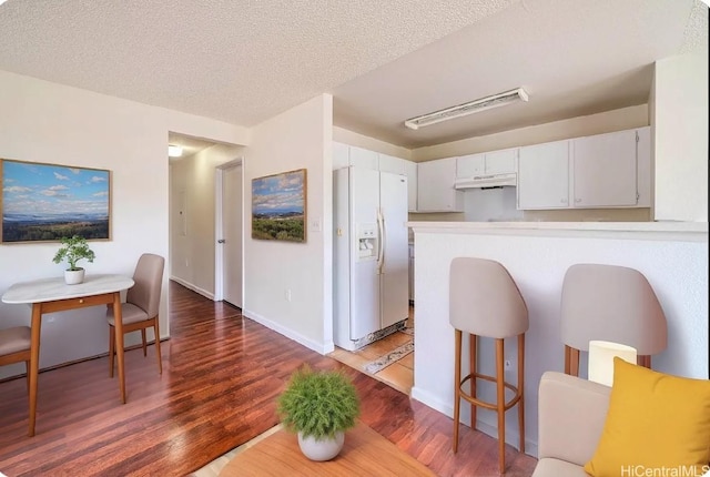 95-1059 Koolani Dr Unit 2, Mililani, HI 96789 - kitchen featuring under cabinet range hood, baseboards, white refrigerator with ice dispenser, white cabinets, and dark wood-style floors
