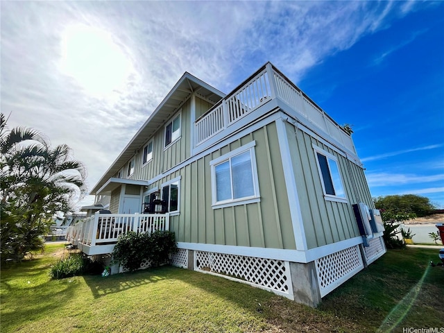 view of side of home featuring board and batten siding, a yard, a balcony, and a wooden deck
