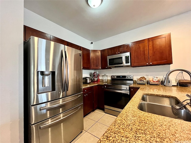kitchen featuring stainless steel appliances, a sink, light tile patterned floors, and light stone counters