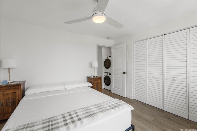 bedroom featuring stacked washing machine and dryer, wood finished floors, ceiling fan, and a closet