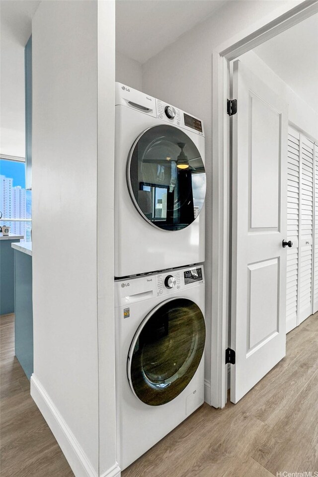 washroom with stacked washer / drying machine, light wood finished floors, and baseboards