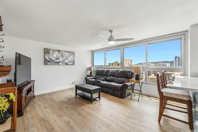 living area featuring a ceiling fan, light wood-style flooring, and baseboards