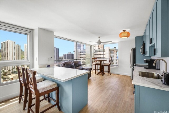 kitchen with a city view, freestanding refrigerator, a sink, blue cabinetry, and light wood-style flooring