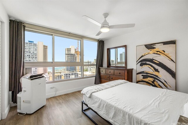 bedroom featuring a view of city, baseboards, wood finished floors, and ceiling fan