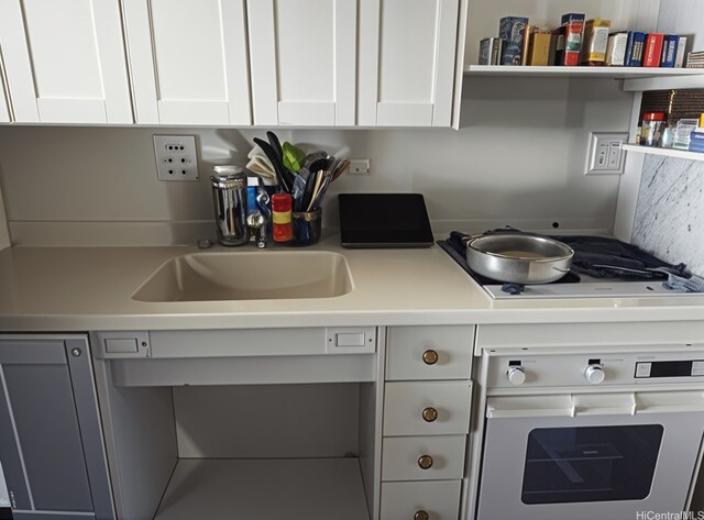 kitchen featuring oven, stovetop, white cabinets, a sink, and light countertops