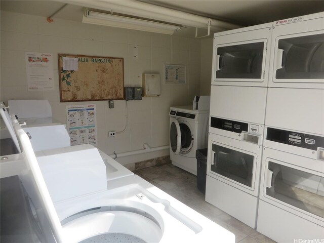 community laundry with stacked washer / dryer, washing machine and clothes dryer, and light tile patterned floors