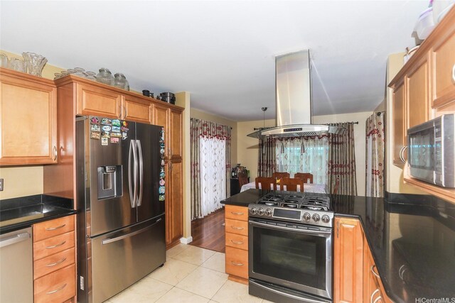 kitchen featuring stainless steel appliances, island exhaust hood, light tile patterned floors, a peninsula, and brown cabinetry
