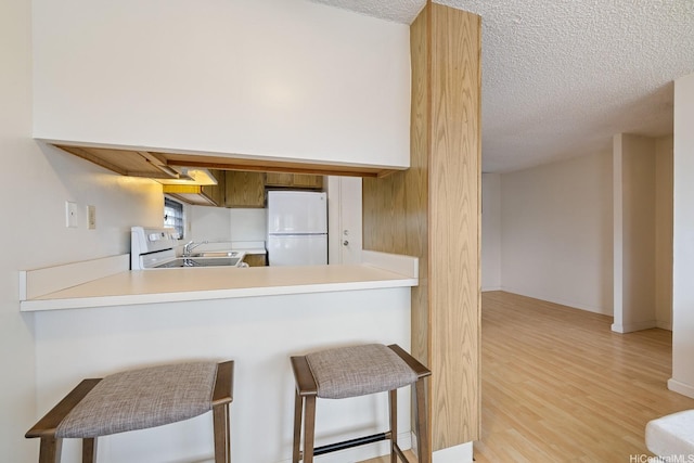 kitchen featuring freestanding refrigerator, a sink, light wood finished floors, a textured ceiling, and a peninsula