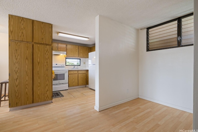 kitchen featuring white appliances, under cabinet range hood, light wood-style flooring, brown cabinets, and a textured ceiling