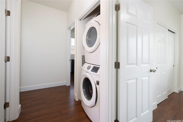 clothes washing area featuring stacked washer / dryer, dark wood-type flooring, and baseboards