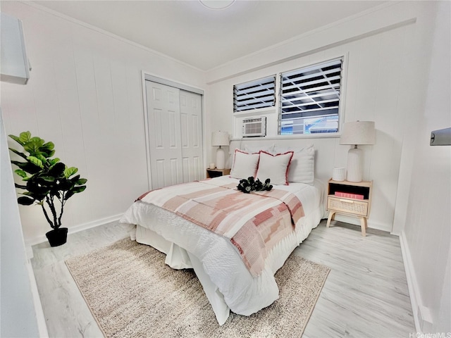 bedroom with light wood-type flooring, baseboards, ornamental molding, and a closet